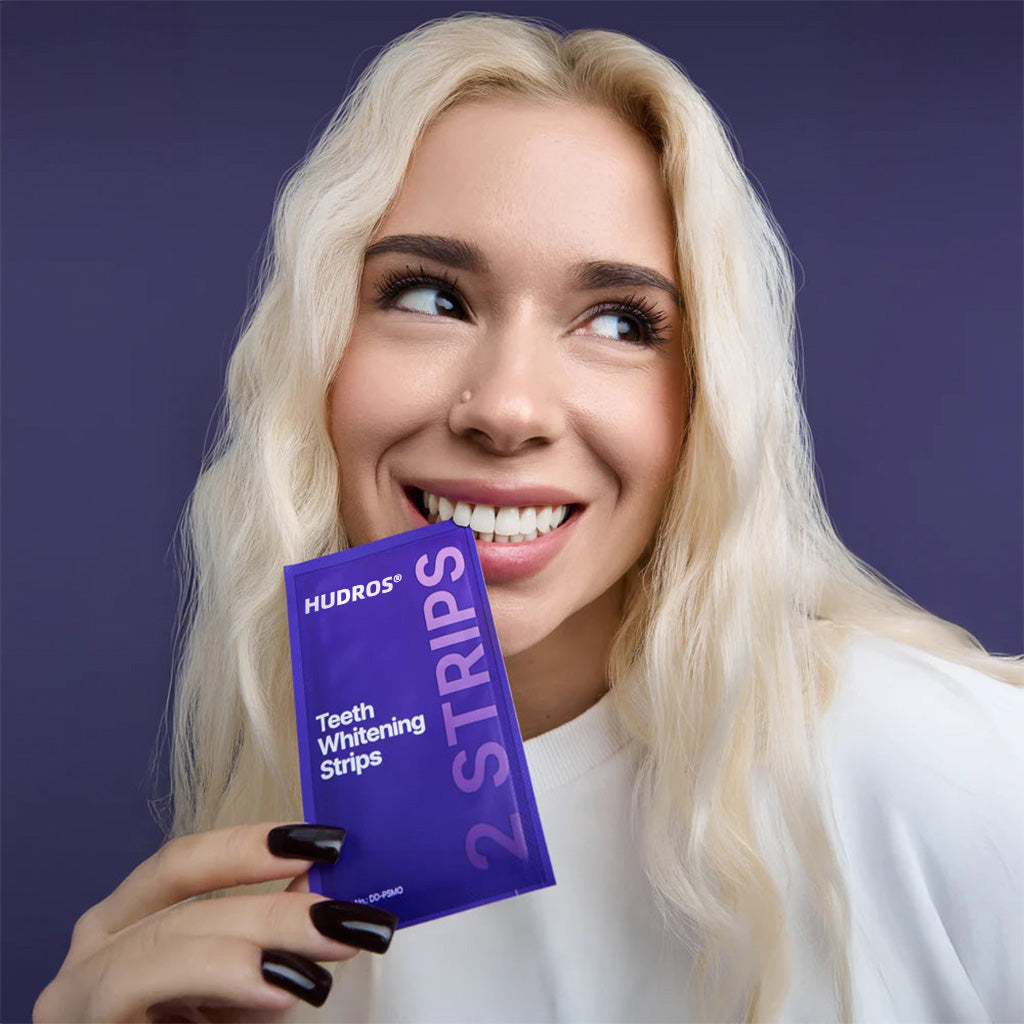 Woman smiling while holding a HUDROS whitening strip sachet